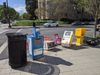 A photo on a D.C. street corner with seven colorful newspaper boxes, five of them are tipped over. 