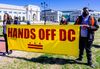 Two people holding a banner that reads Hands Off D.C. 