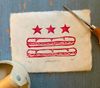 A print of the D.C. flag with sandwiches replacing the bars sits on a table next to tools. 