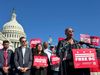 A photo showing Ayanna Pressley speaking into microphones outside of the U.S. Capitol with a crowd gathered behind her. The podium, and several crowd members, bear signs that say "Free DC"