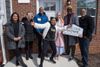 A group of people of different races stand in front of a brick house, holding a sign that says WELCOME HOME.