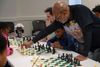 Vaughn Bennett leans over a chess board, teaching kids at a table how to play the game.