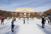 People ice skate on a rink with a museum in the background.