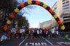 A crowd of runners lined up at a starting line, under a Thanksgiving-themed arch of balloons.