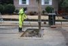 A person in a yellow suit leans over a hole in the concrete to update old gas pipes.