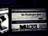 A black and white photograph of a laptop screen with The Washington Post homepage, and Jeff Bezos in the background.