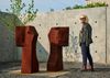 A person stands next to a sculpture in a Brutalist outdoor space