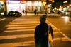 A person in a hat stands in front of a crosswalk on Columbia Road NW in D.C.'s Adams Morgan at night.