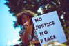 Black woman in zebra top holding a sign that says No Justice No Peace