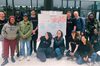 Thirteen people pose around a white poster with blue and red dots on the page in three sections, there's a cluster of red dots on the right showing people left feeling more informed. 