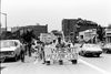 A black and white photograph of people marching down Columbia Road holding signs, including one that reads: "We're not moving out."