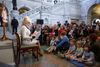 A photo of Dolly Parton wearing white sitting in a chair holding a book and reading to kids.