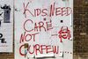 Wheatpasted sign on a wall reading "Kids Need Care Not Curfew"