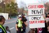 A hand-made sign reading Statehood Now! Only Statehood with police officers in front of a crowd in the background.