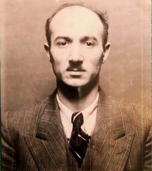 A sepia image of a man in a 3 piece suit. He has a mustache.