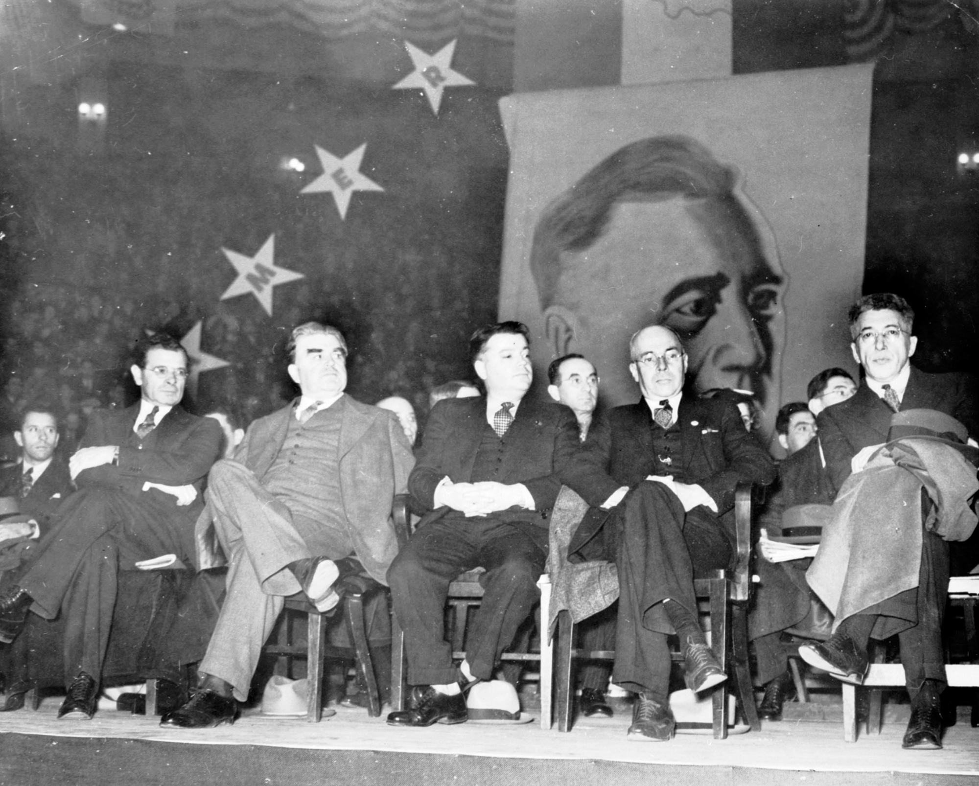 Sidney Hillman, John L. Lewis, David Dubinsky, and B. C. Vladeck at an American Labor Party event sitting on a stage in front of a large portrait of FDR