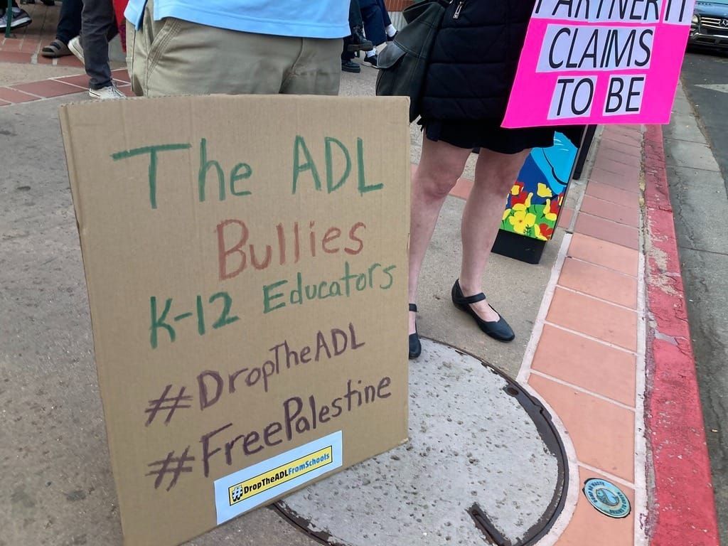 2 signs from a protest, 1 reads "the adl bullies k-12 educators #droptheadl #freepalestine" and the other is cut off