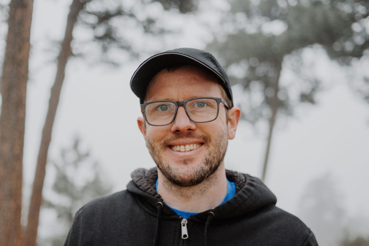 A portrait photograph of Gavriel, who is wearing rimmed glasses, a black hoodie, and a black messenger hat