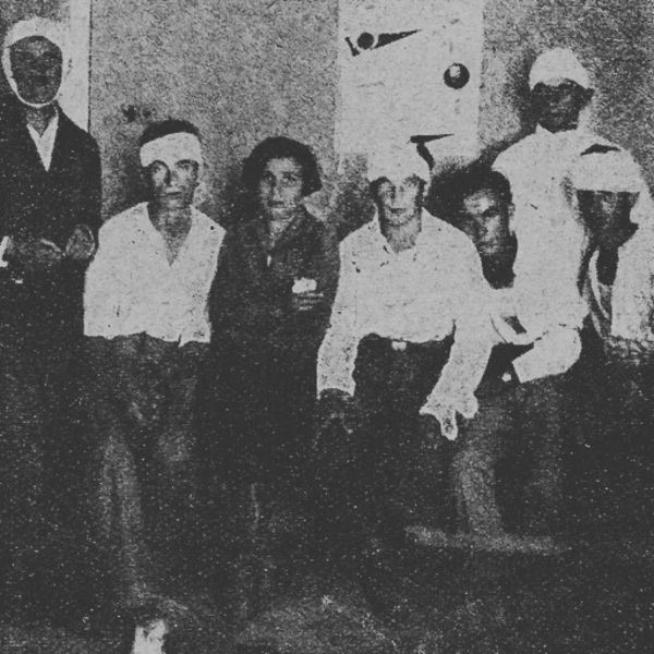 Six bandaged men and a woman stand along a wall lookin at the camera