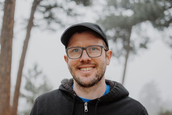 A portrait photograph of Gavriel, who is wearing rimmed glasses, a black hoodie, and a black messenger hat
