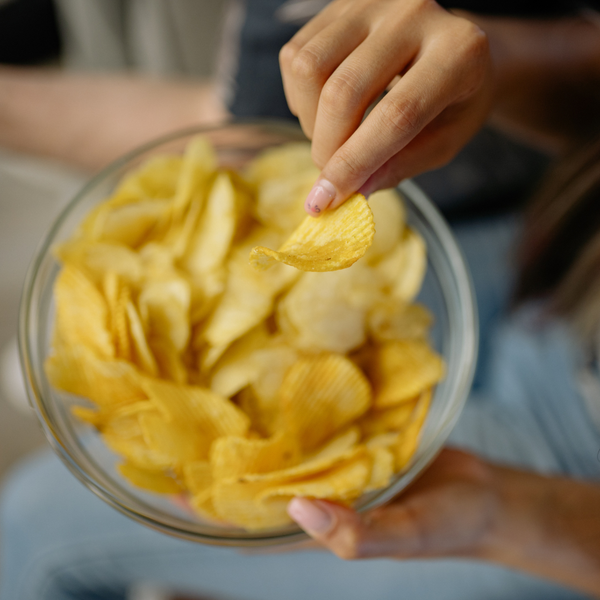 Mano che prende una patatina da una ciotola trasparente piena di snack, immagine simbolica per una riflessione sulla comunicazione alimentare, sui gesti di consumo e sulla responsabilità dell