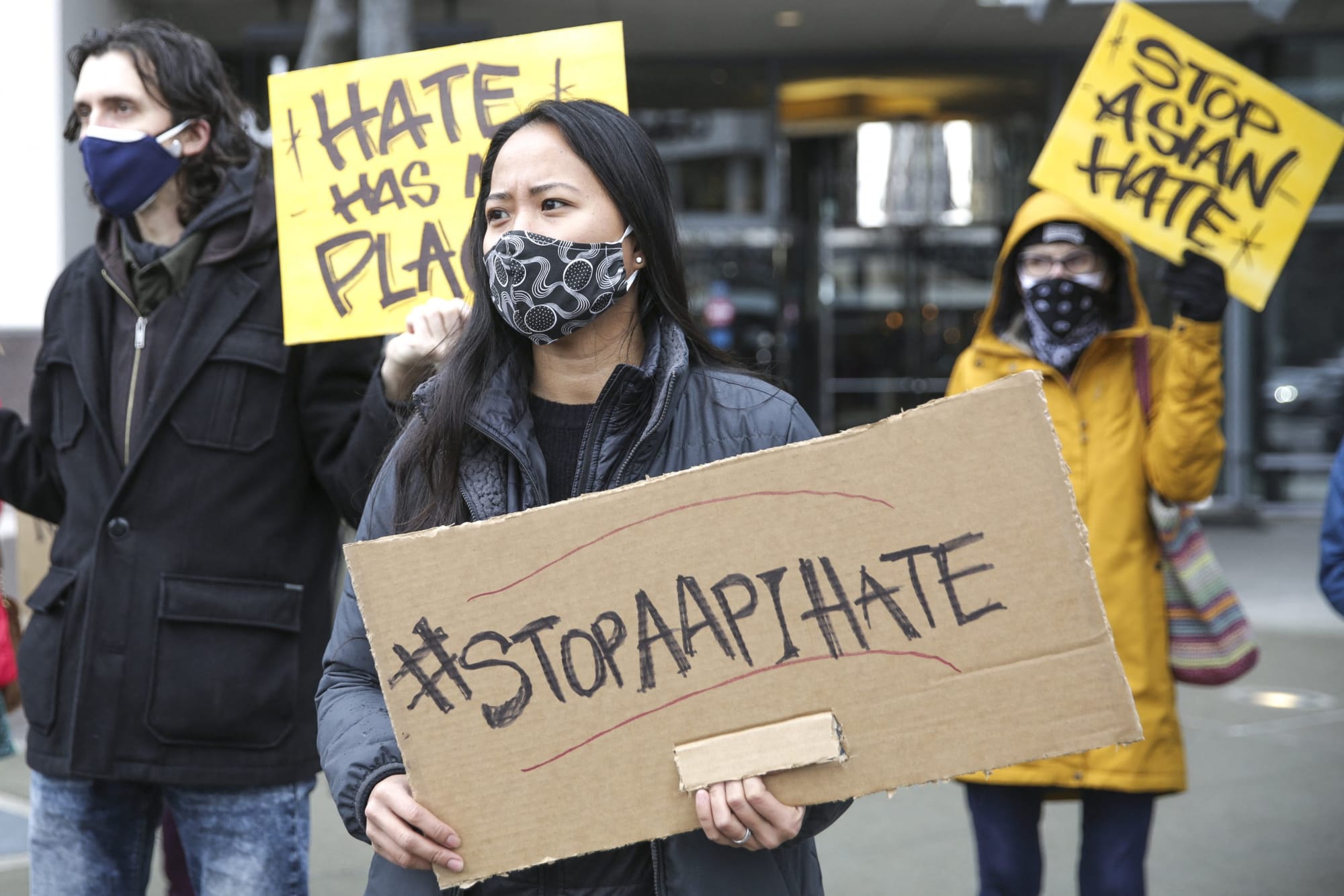 an asian woman wearing a mask holds a sign reading "#StopAAPIHate"