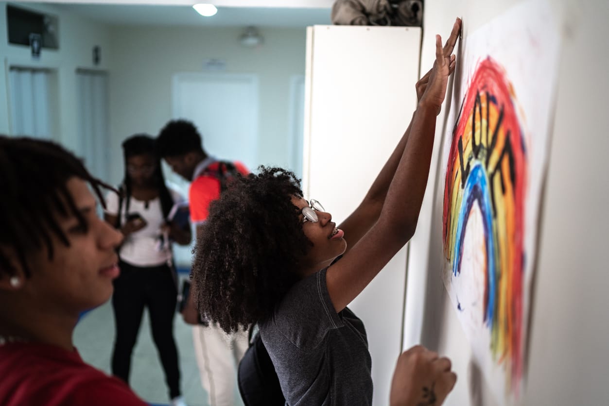 Black teens taping a rainbow poster to a wall inside of a room