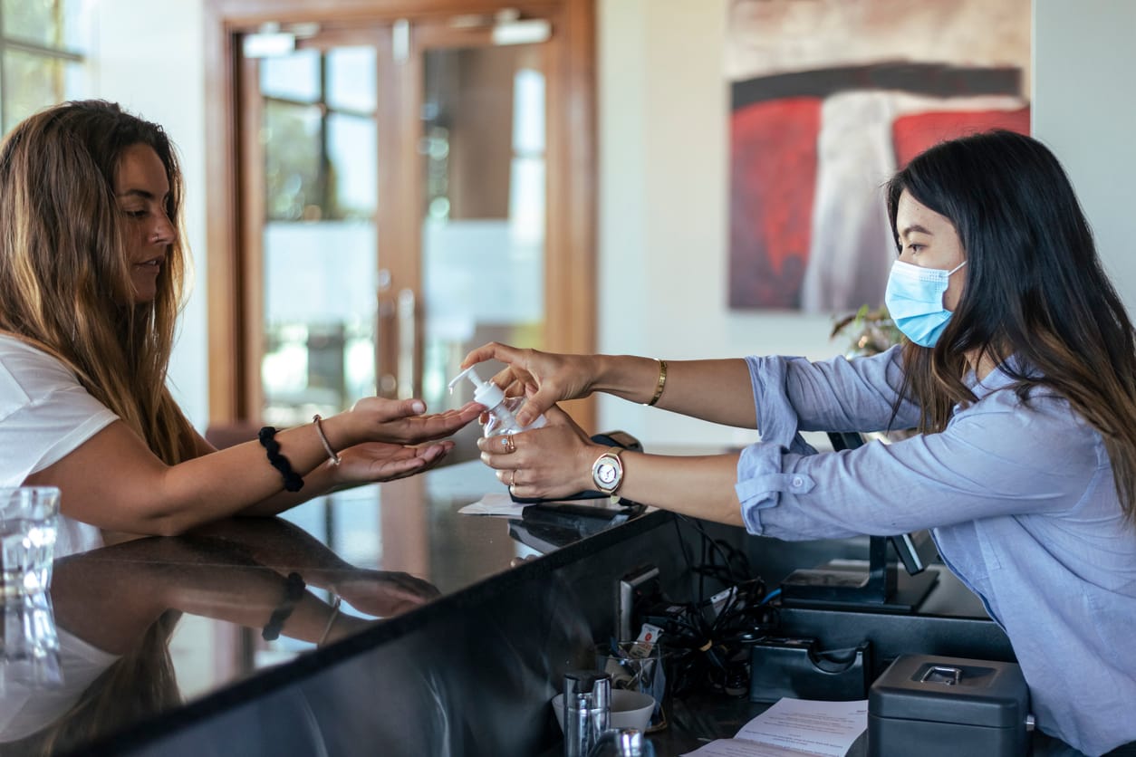 Asian waitress wearing face maskprovides white customer with hand sanitizer