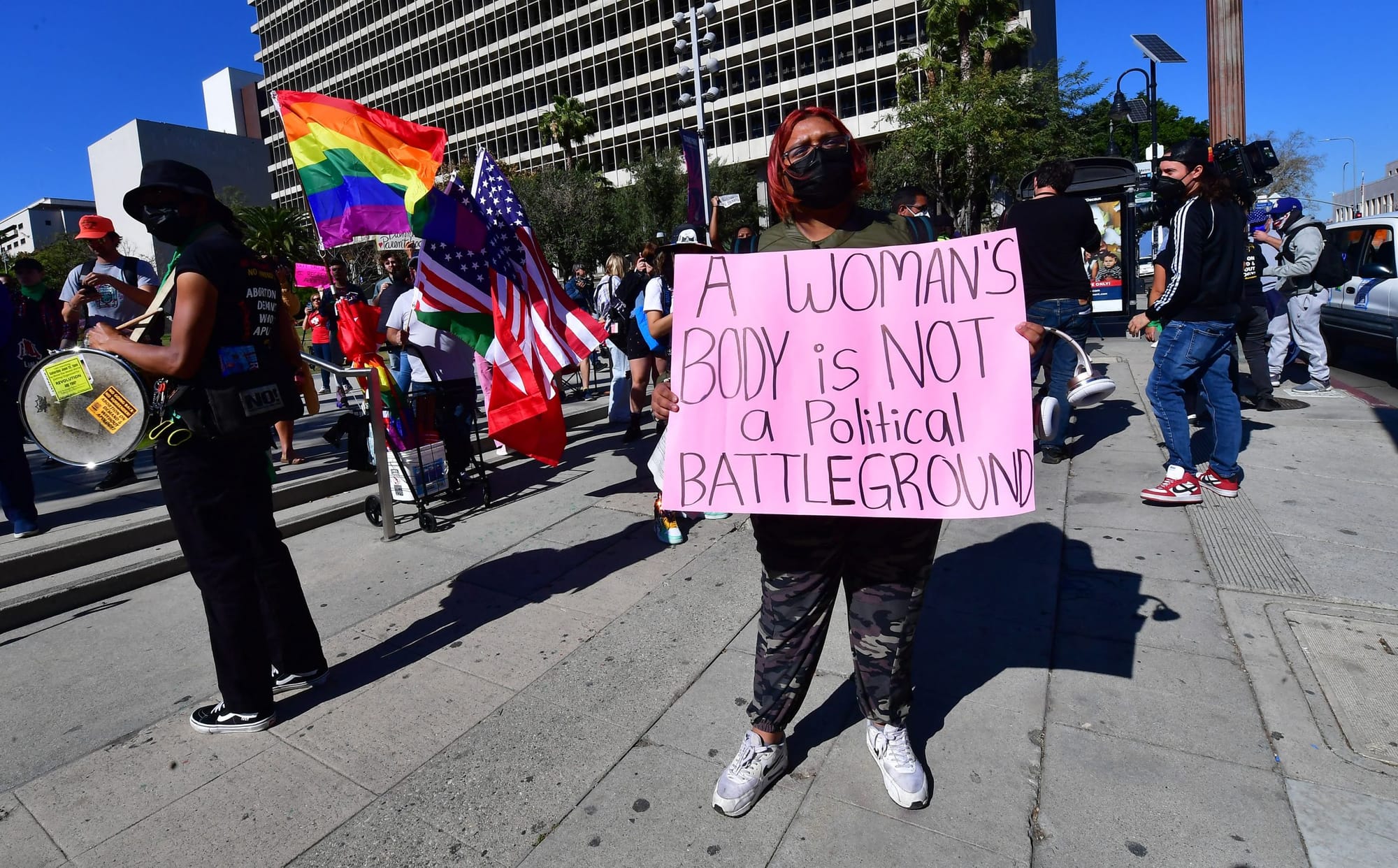 a black woman wearing a mask holds up a sign reading "A woman's body is not a political battleground"