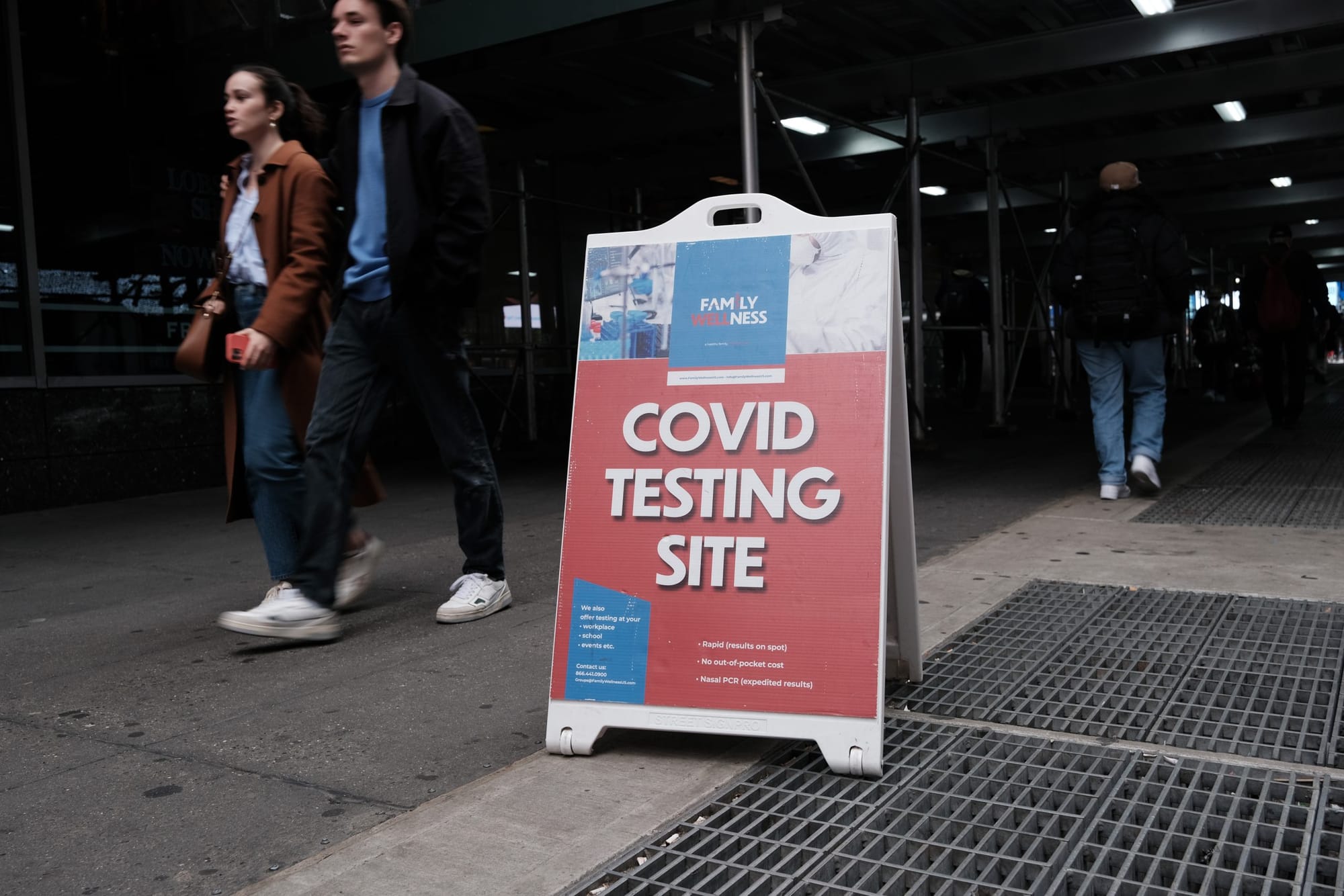 people walk past a sign for a COVID testing site