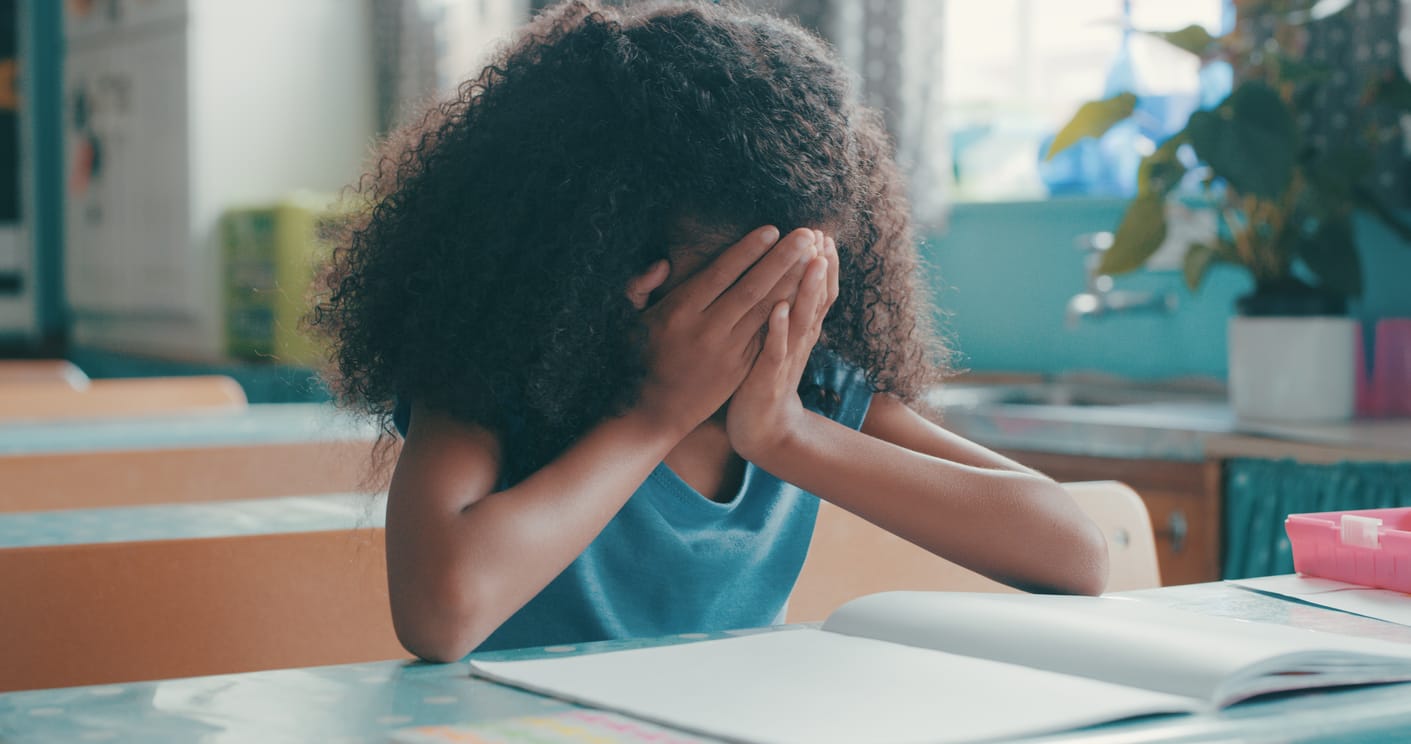 a young Black girl looking frustrated while doing her schoolwork in class