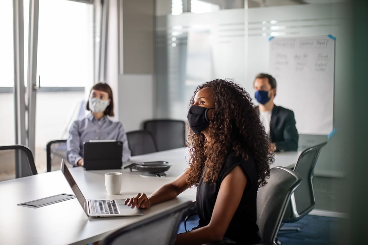Team of business professionals wearing face mask sitting in office boardroom during a meeting. Business people having meeting
