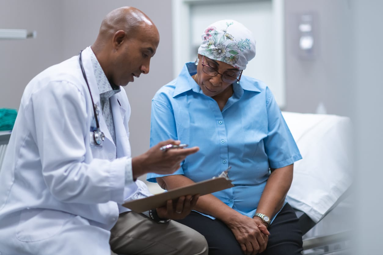 A black senior woman with cancer is at a medical consultation. She is wearing a scarf on her head to hide her hair loss. The