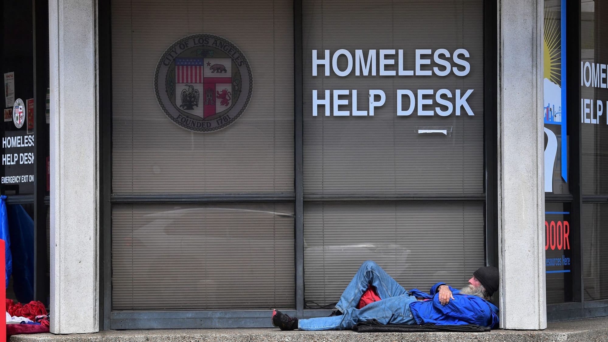 a houseless man lies on the ground outside the window for the Homeless Help Desk