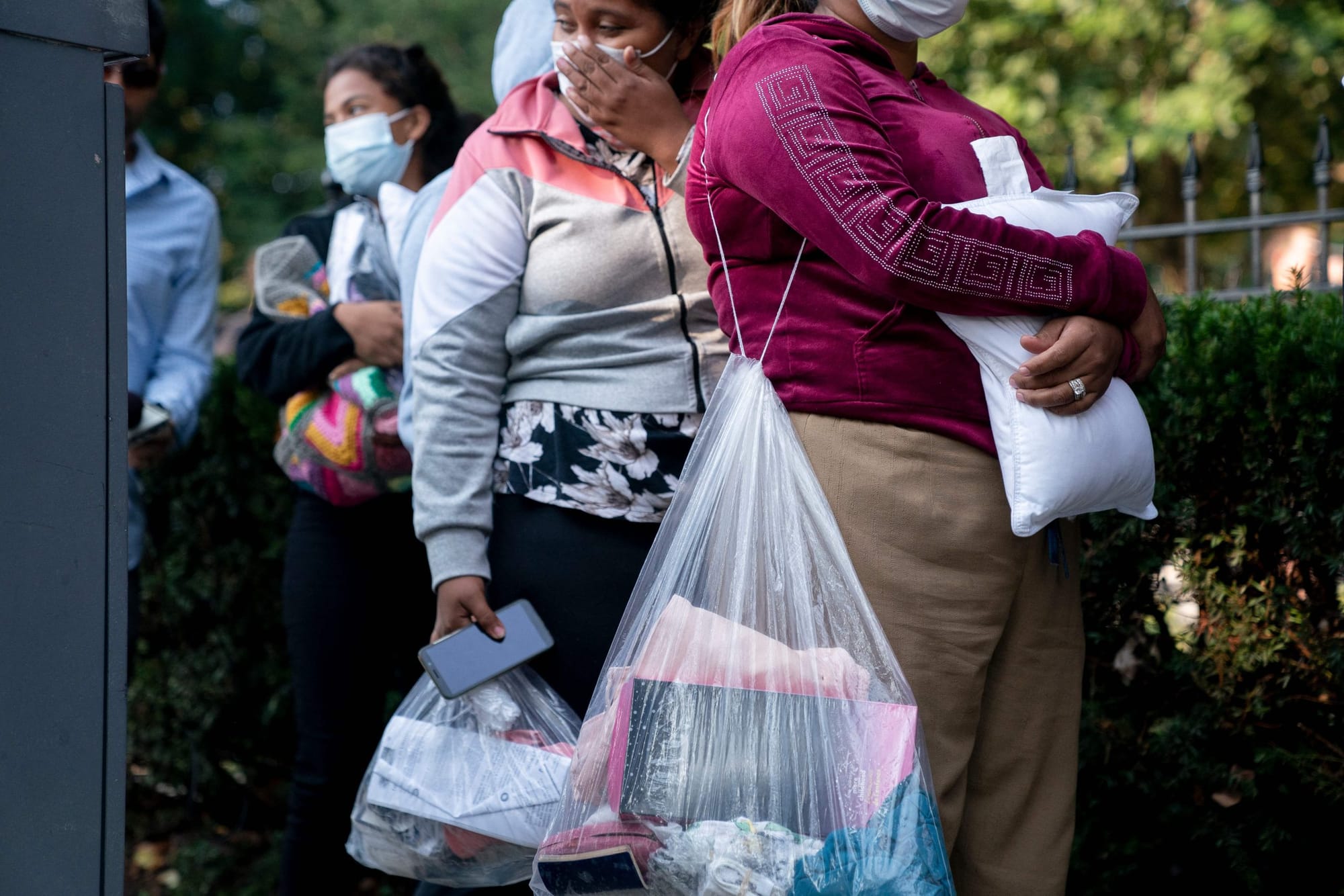 Venezeulan asylum-seekers in long pants and light jackets hold clear plastic bags of their belongings while they wait on the