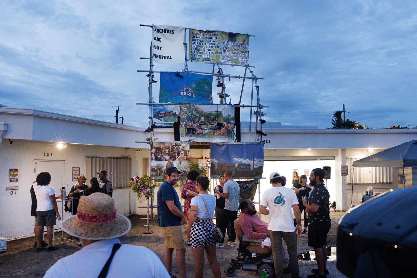 color photograph of people standing outside engaging with an art display in Little Haiti, Miami. Metal scaffolding holds up b