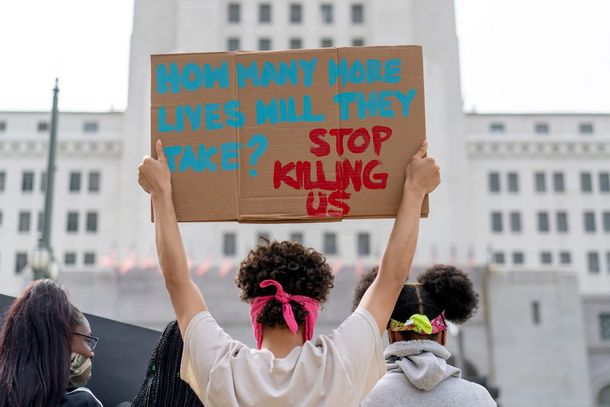 color photograph of a protest outside City Hall in LA, a white building with small rectangular windows and a middle section t