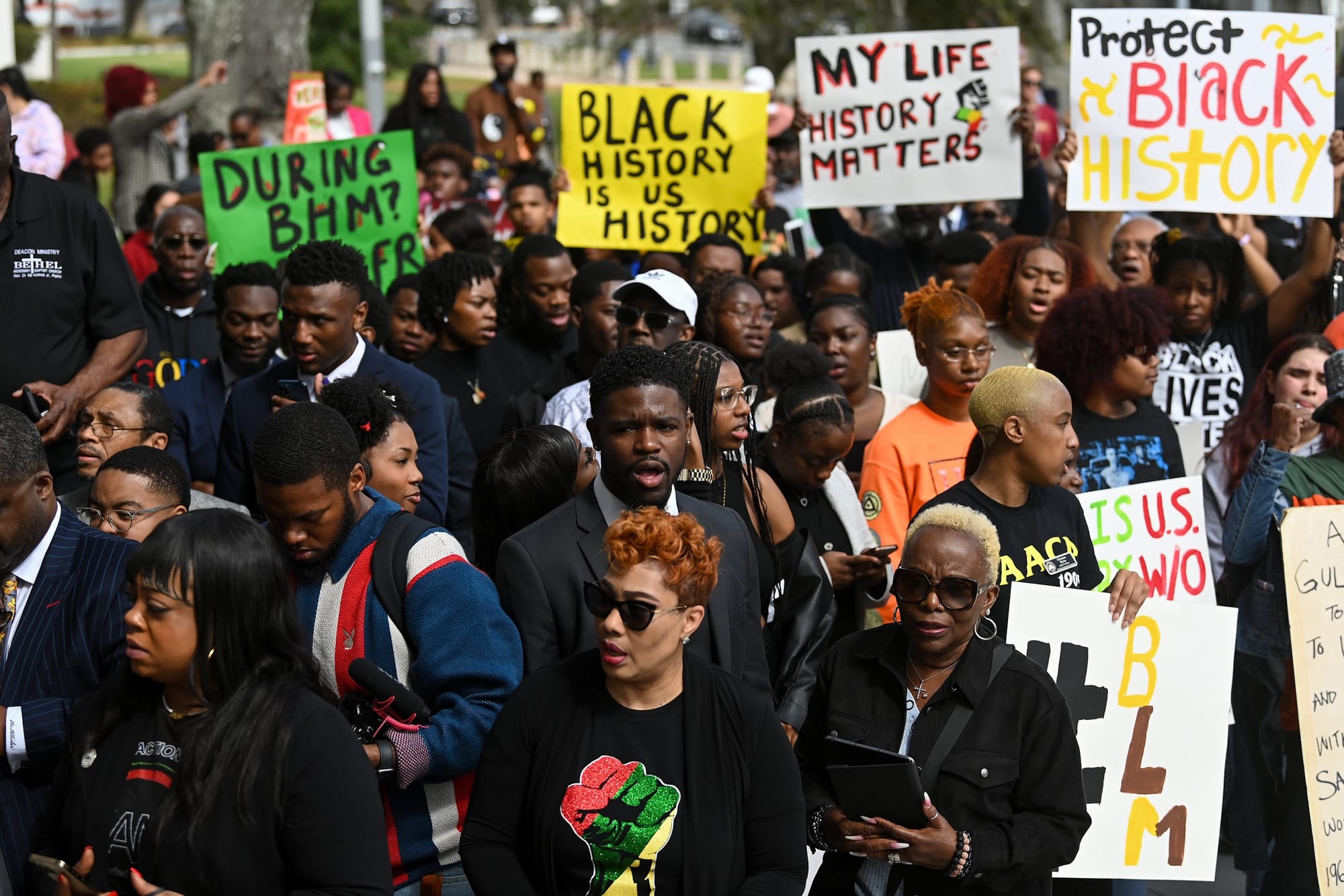 color photograph of an outdoor protest of mostly Black people who are holding paper signs with slogans like "Black history is