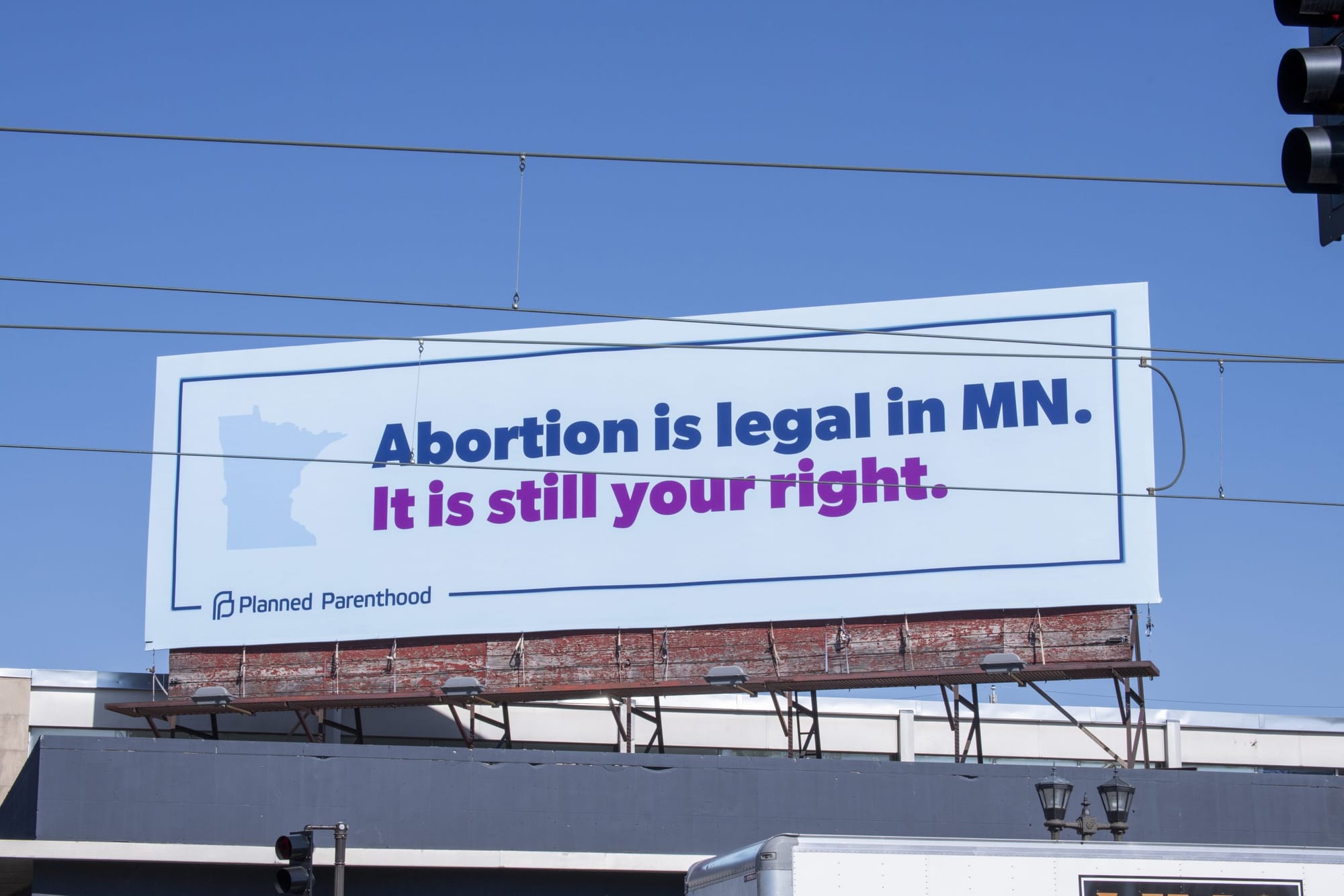color photograph of a planned parenthood ad on a white billboard atop a building roof that reads "abortion is legal in MN" in