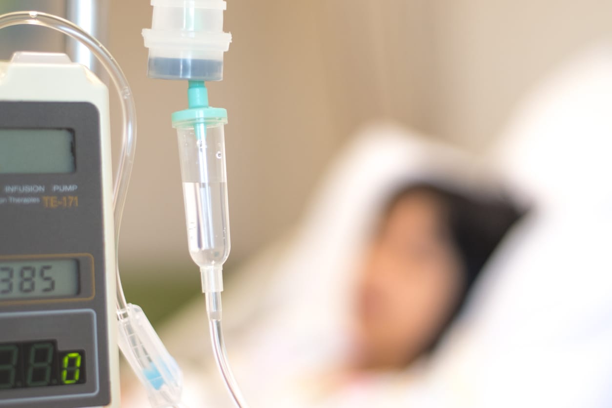 young person with black hair with IV line in hand sleep on hospital bed.