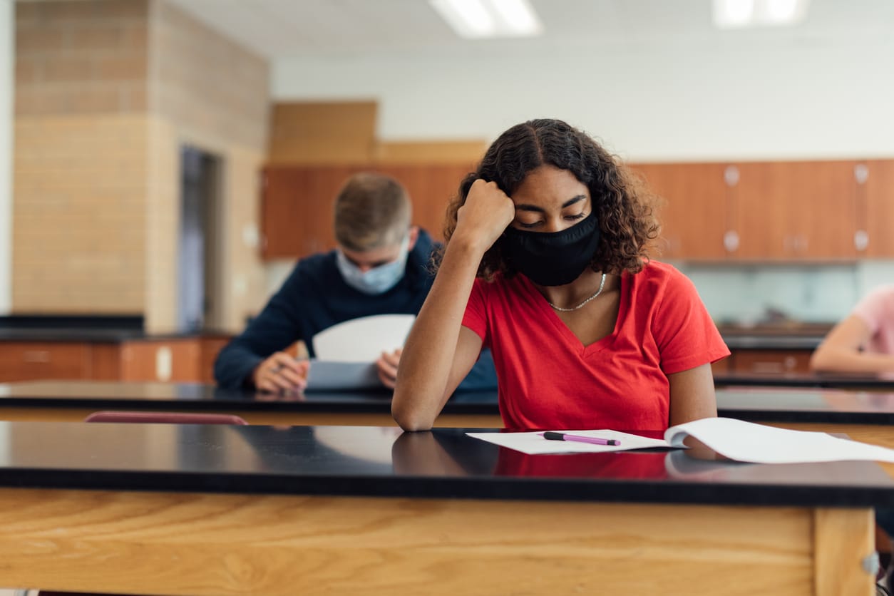 stock photo of a black high school student with shoulder-length curly hair wearing a red shirt sitting in a science classroom