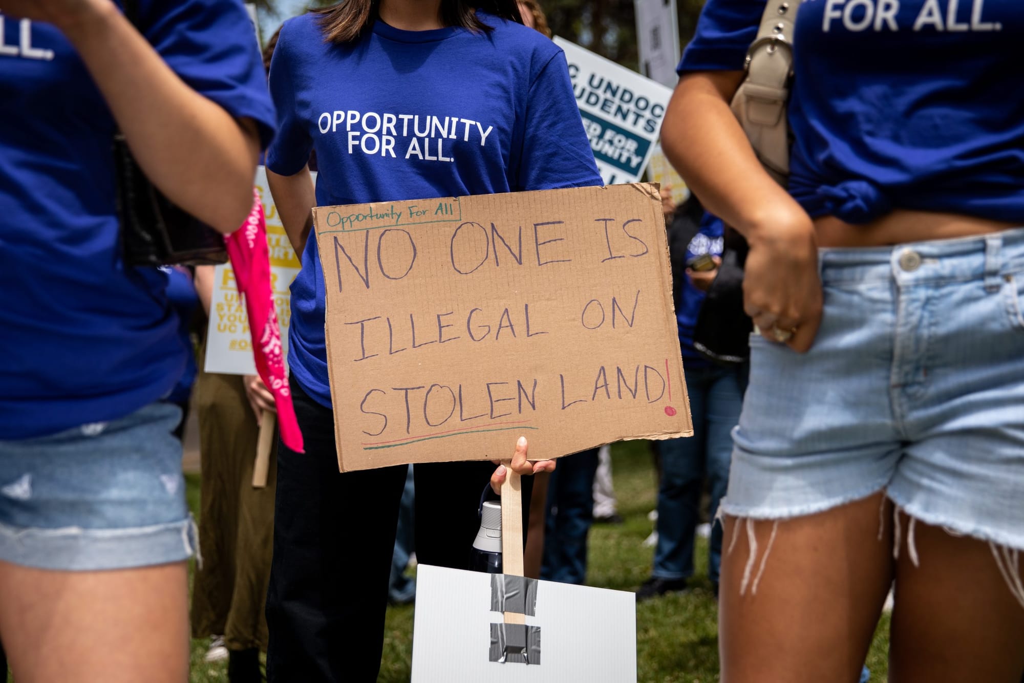 color photograph of the abdomens and upper legs of three protesters. they all wear dark blue t-shirts. the protester in the m
