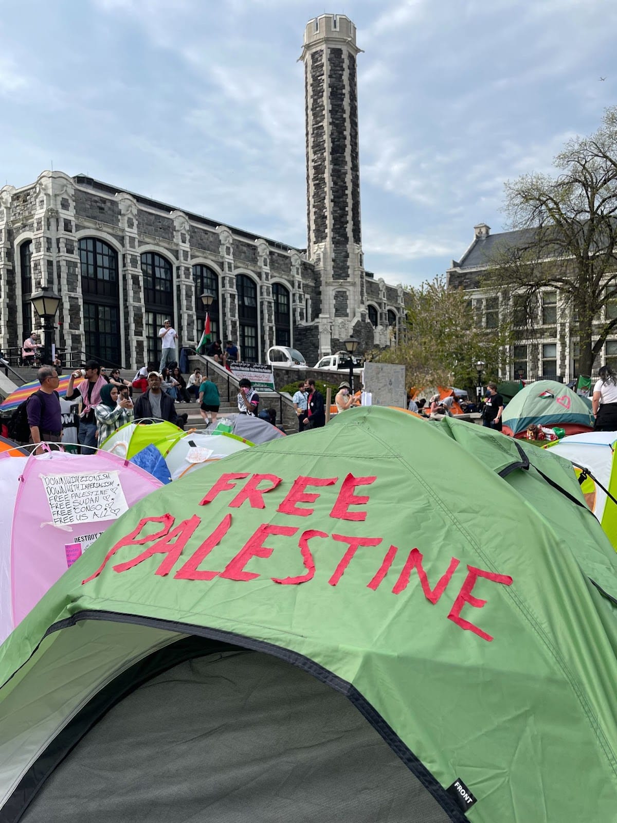 color photograph of tents on a university lawn with red cloth letters reading "Free Palestine" on the green tent in the foreground