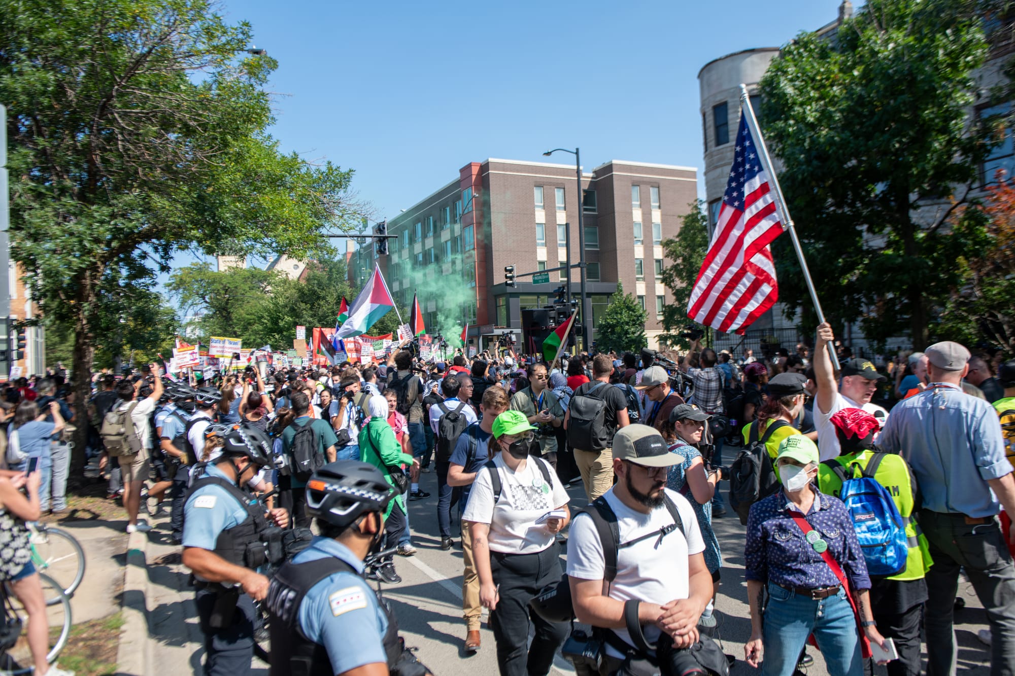 color photograph of people walking down a street holding American and Palestinian flags