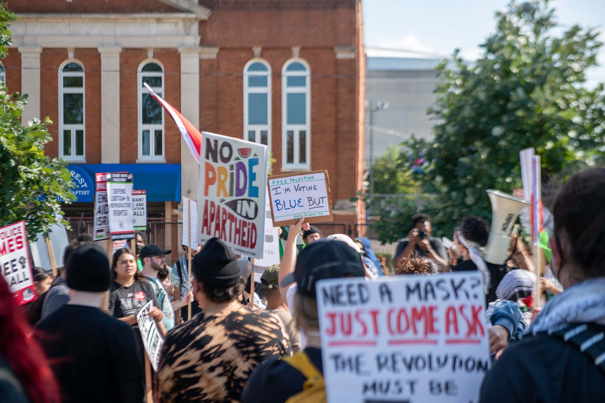 color photograph of people holding up pro-Palestine signs and signs encouraging masking