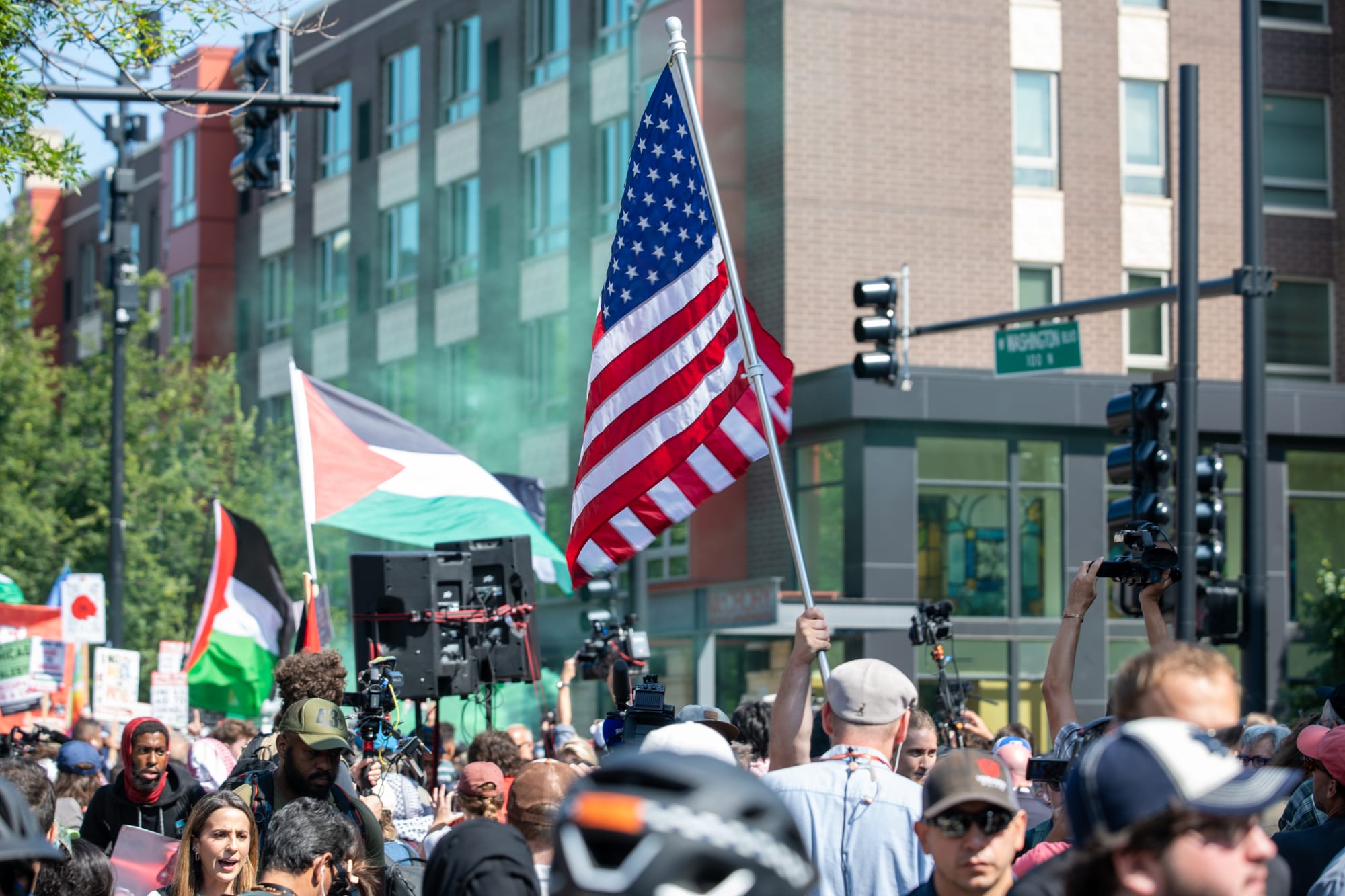color photograph of people holding American and Palestinian flags as they walk down a street