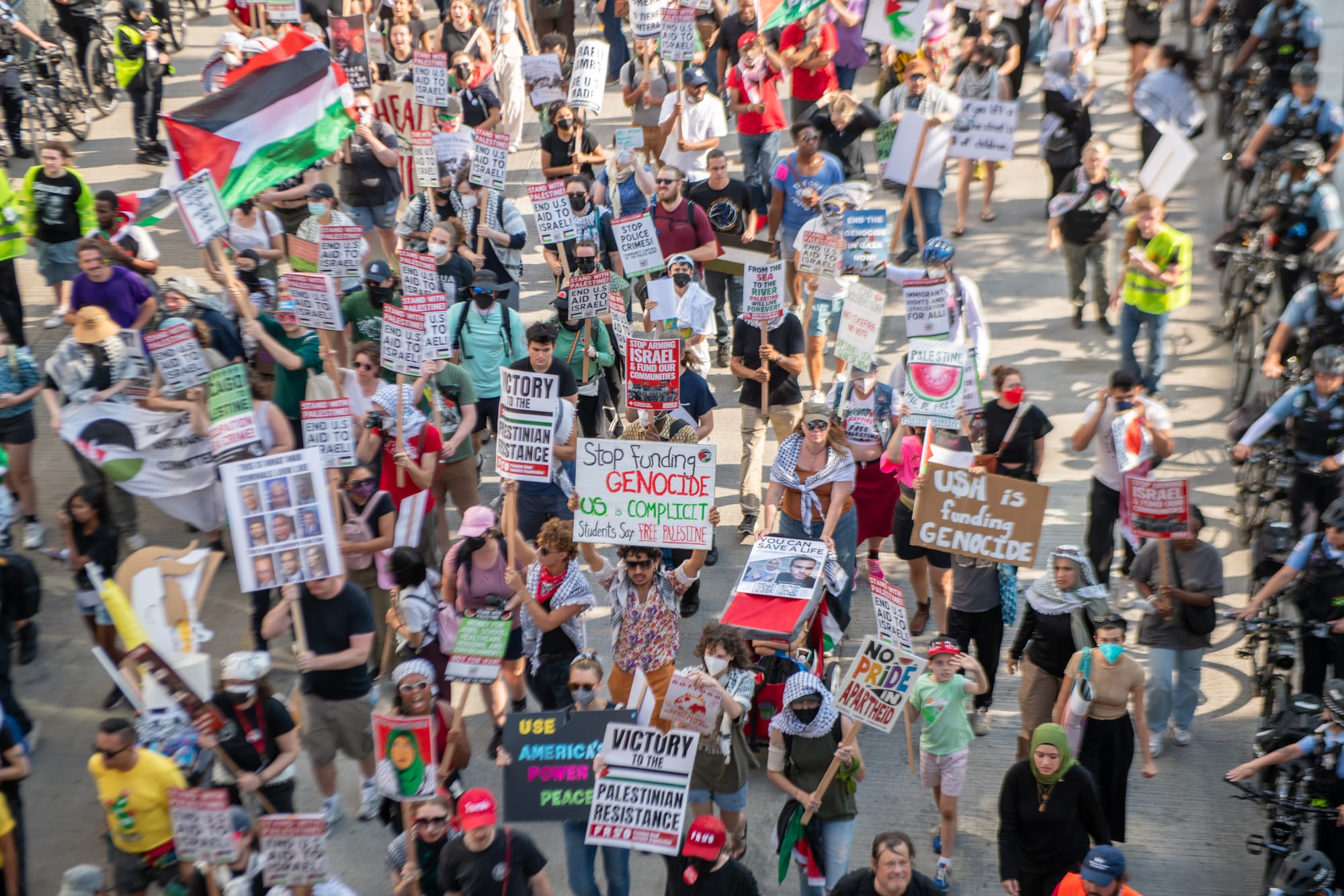 color photograph aerial close-up of about a hundred protesters walking down the street. police line both sides of the street