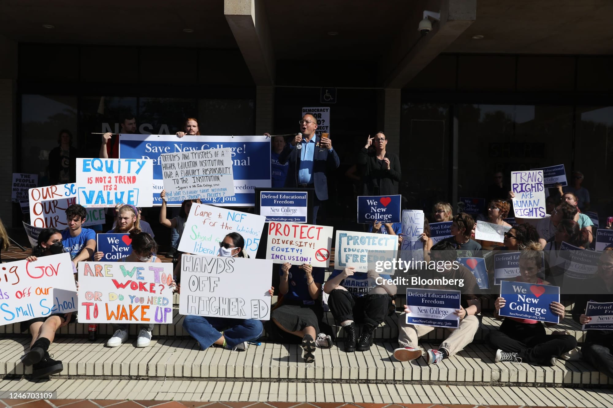 Several students sit while holding protest signs in support of New College of Florida.