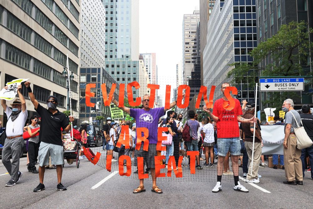 three people hold up a sign reading "eviction is violence" during a protest on a city street