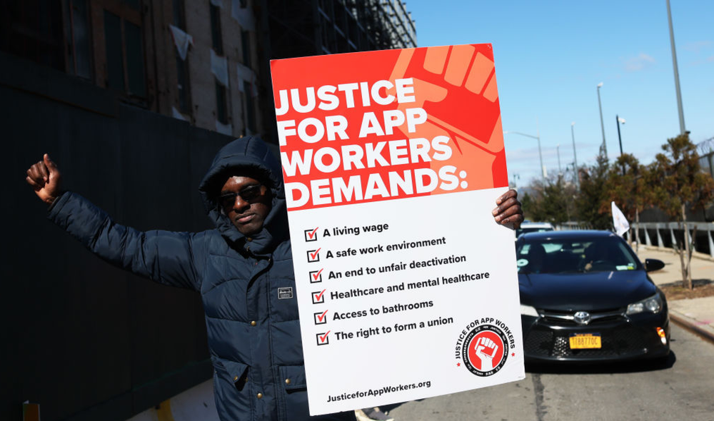 Man holding a protest sign in support of app workers' rights.